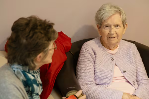 Two older women sitting and talking together on a sofa at home