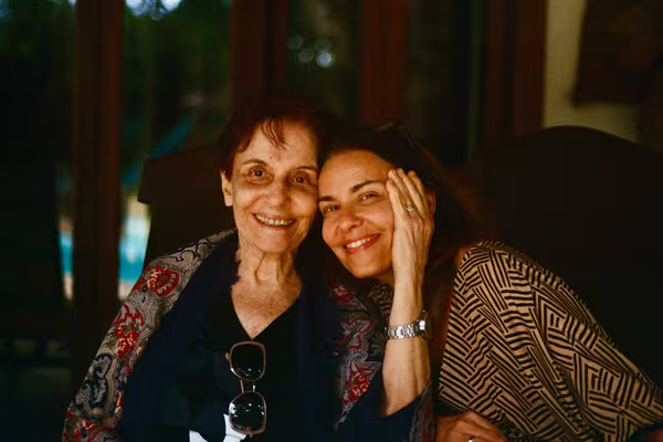 An older mother and her adult daughter sitting cheek to cheek, smiling together