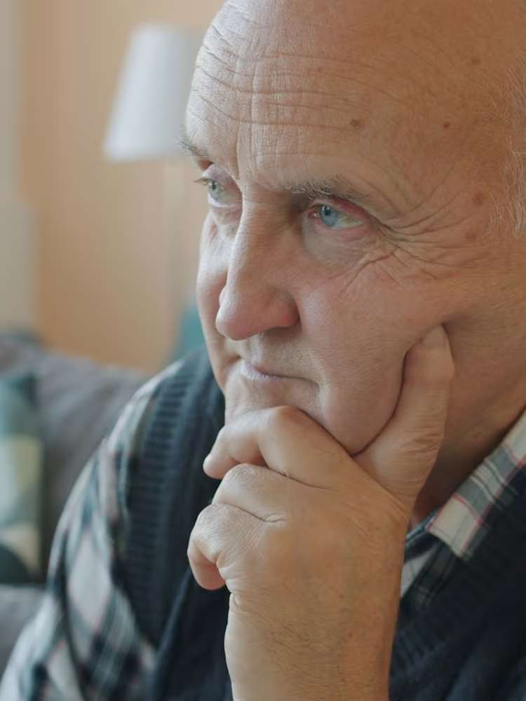 A close-up of an older man resting his cheek on his hand, gazing away and looking worried