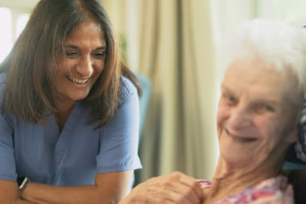 A smiling care worker in blue scrubs sharing a warm moment with an older woman at home