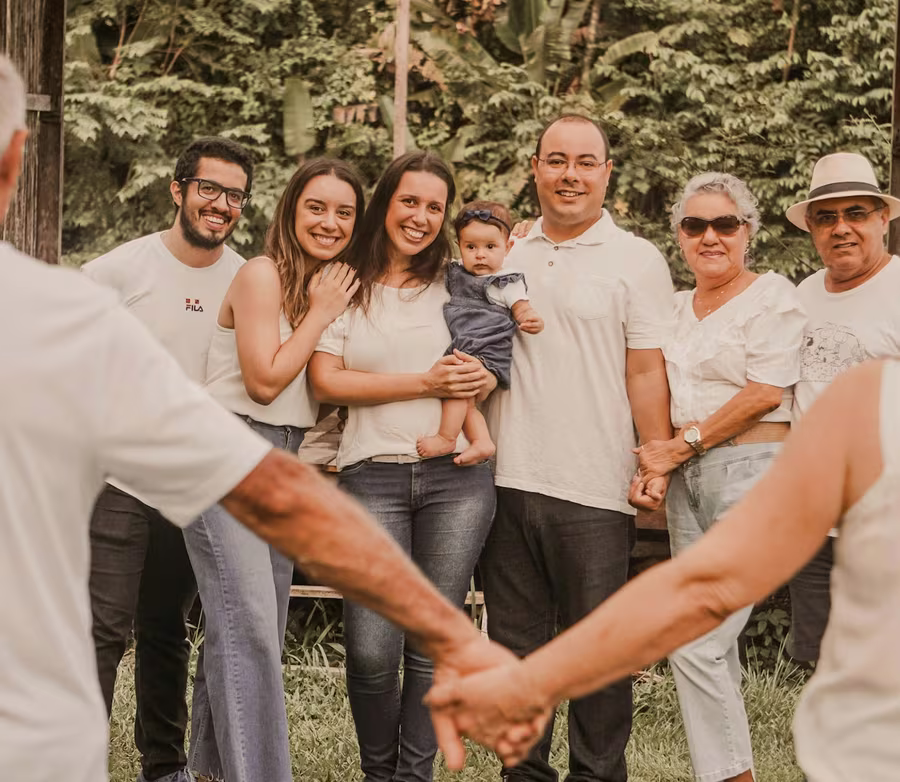 Three generations of one family gathered outdoors, smiling, holding hands in a circle