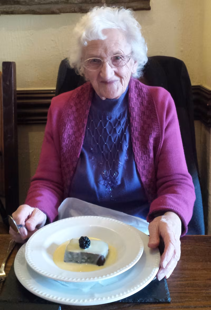 Graham's mum smiling at a table with a dessert on the plate in front of her