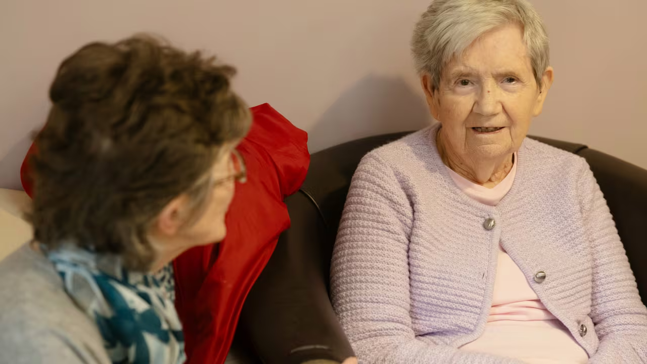 Two older women sitting and talking together on a sofa at home