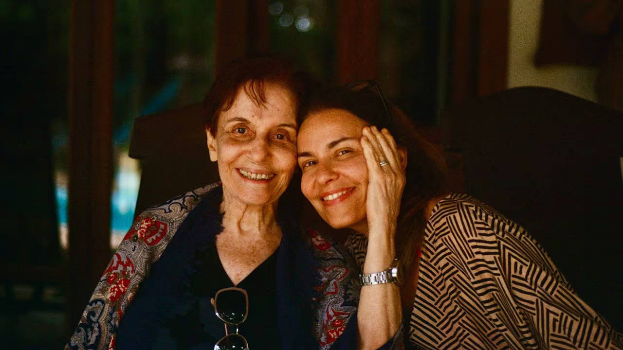 An older mother and her adult daughter sitting cheek to cheek, smiling together